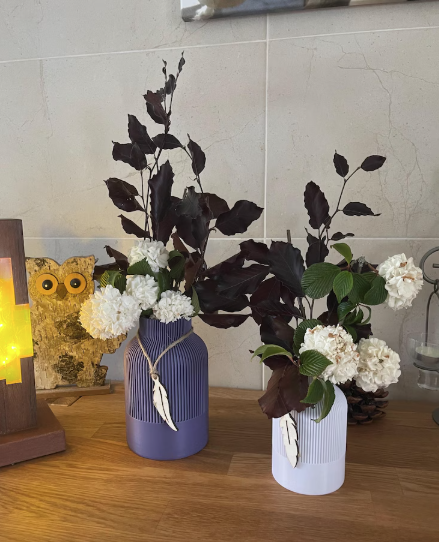 Zwei Vasen mit weißen Blumen und dunkelrotem Laub auf einer Tischoberfläche.